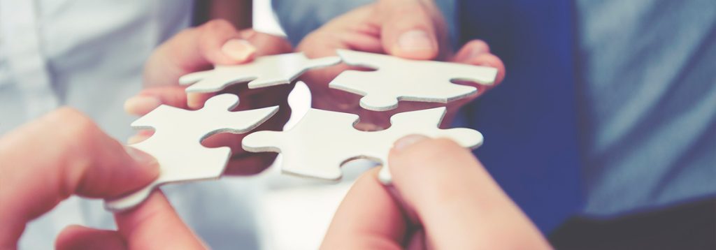 Pessoas unindo peças de um quebra-cabeça, simbolizando integração e trabalho em equipe
