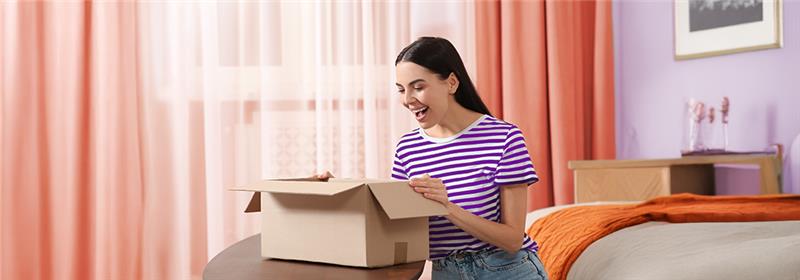 Cliente sorrindo ao abrir caixa, satisfeita com entrega rápida e frete transparente.