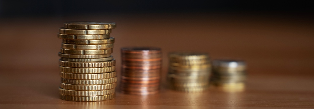 Pilhas de moedas de diferentes valores organizadas sobre uma superfície, simbolizando arrecadação, tributos e os impactos financeiros da Reforma do ICMS na economia.