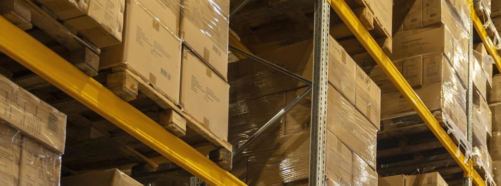 Corredor de armazém industrial com prateleiras altas e organizadas, repletas de caixas e pallets empilhados